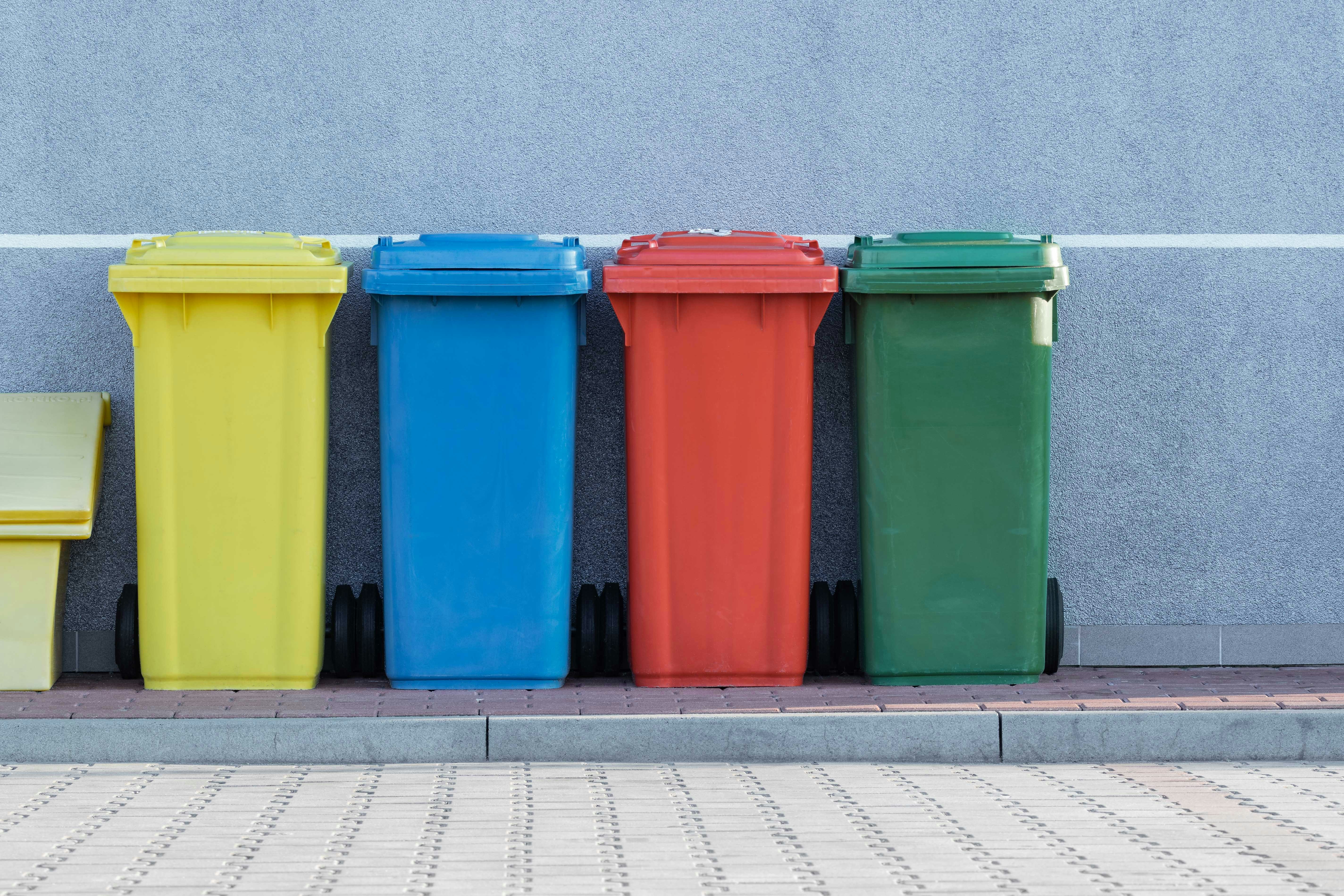 four assorted-color trash bins beside gray wall